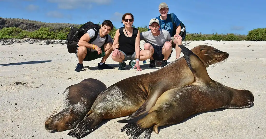 Yacht La Pinta guests posing with sea lions on Santa Fe Island, Galápagos.
