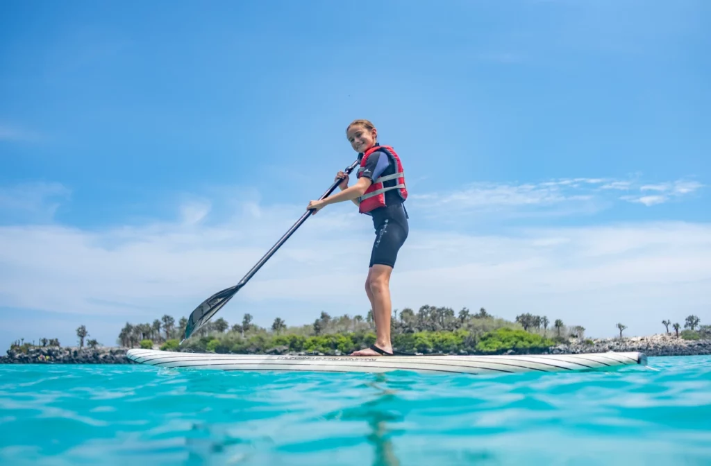 Woman paddleboarding in shallow turquoise waters near a small vegetated island in the Galapagos on a sunny day.
