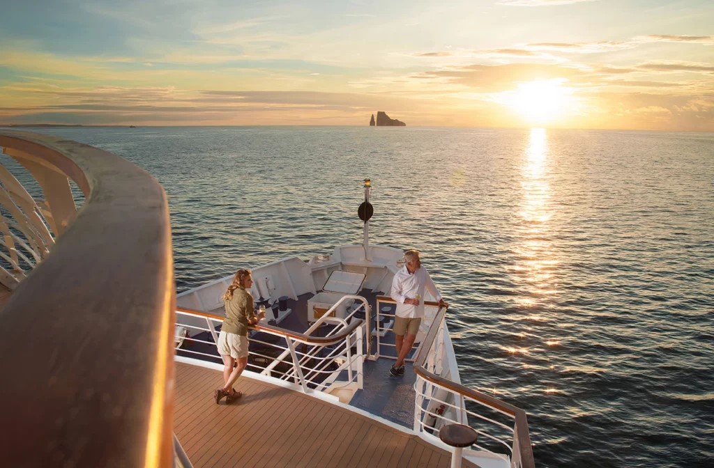 Couple enjoying a golden sunset from the top deck of Yacht La Pinta with Kicker Rock silhouetted on the horizon in the Galapagos.