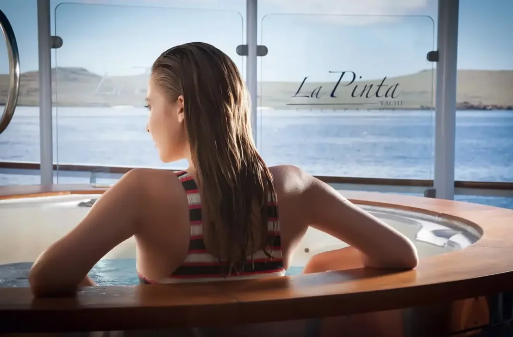 Woman relaxing in the hot tub aboard Yacht La Pinta with panoramic ocean views through the window.