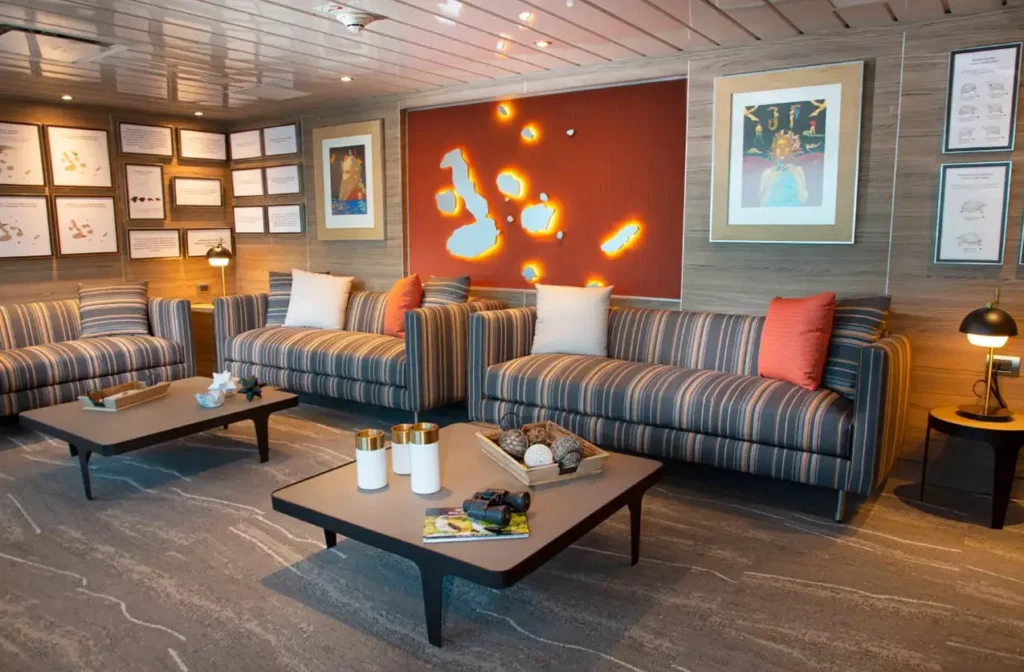 Cozy lounge area aboard Yacht La Pinta featuring striped sofas, orange accent wall with backlit artwork and warm ambient lighting.