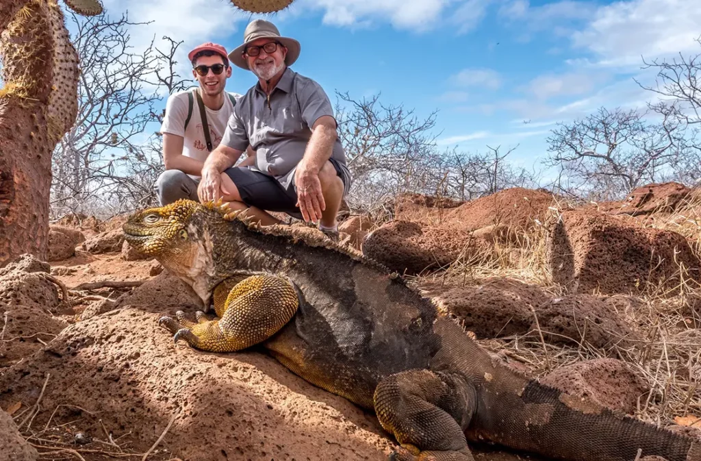Two guests posing with a Galapagos land iguana on North Seymour Island